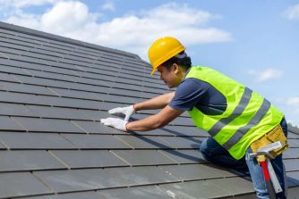 Roof repair, worker with white gloves replacing gray tiles or sh